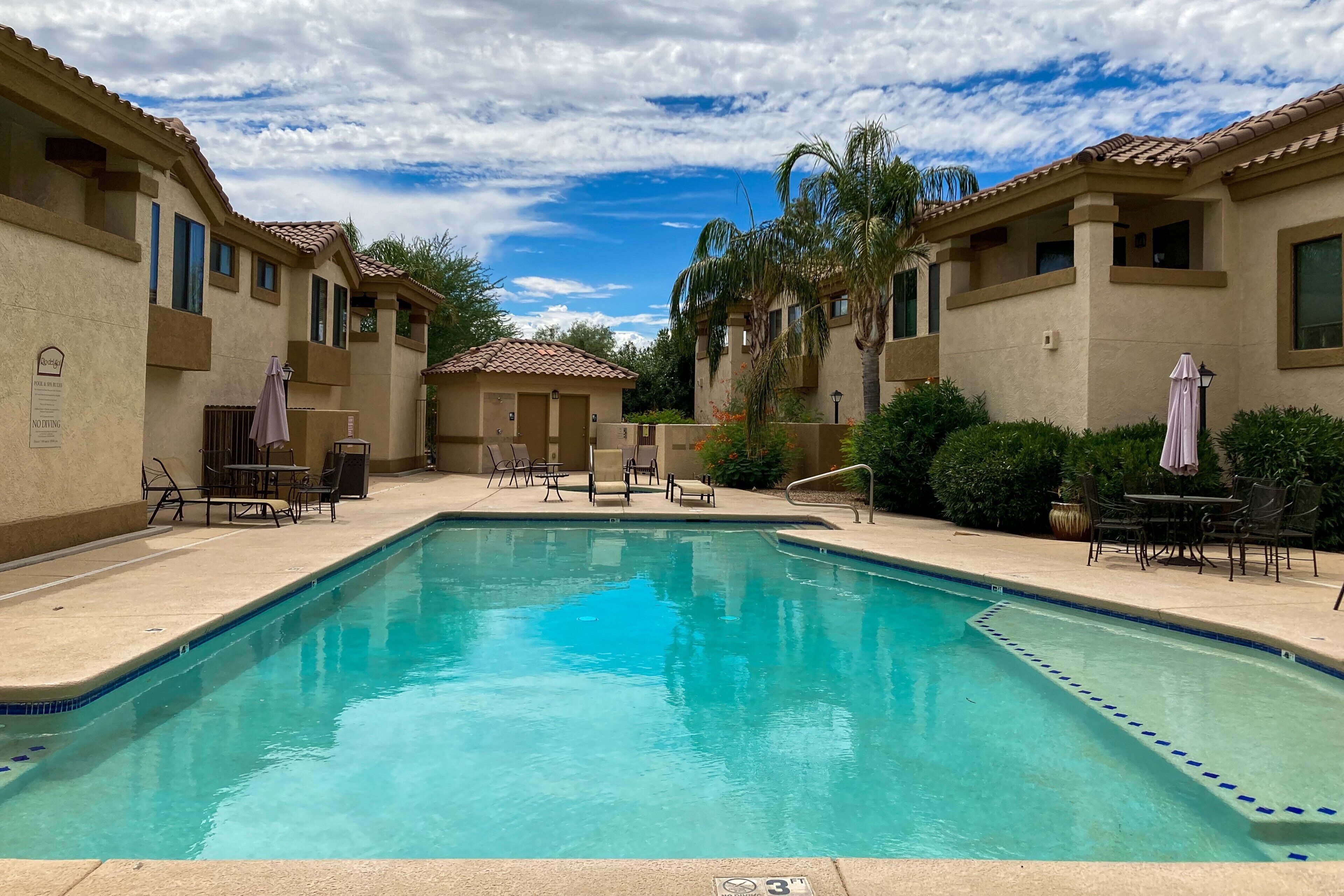 A swimming pool with lounge chairs and umbrellas, surrounded by buildings with a tiled roof.