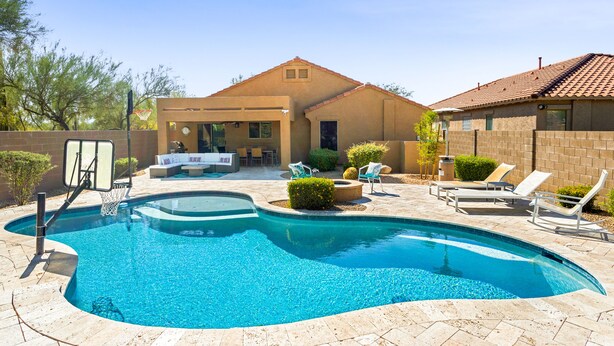 A swimming pool with a basketball hoop, lounge chairs, and a patio area with a table and chairs. - Pristine Desert Ridge home with a pool & backyard oasis - dog-friendly (Phoenix)