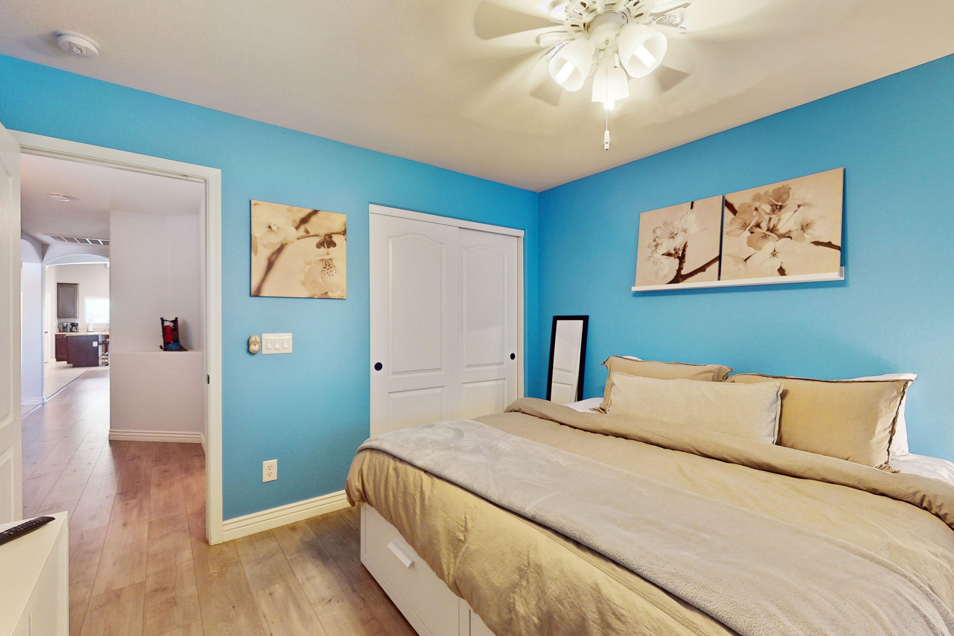 A bedroom with a bed, a ceiling fan, and two wall-mounted flower paintings.