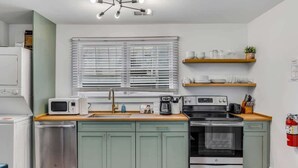 A compact kitchen with a microwave, coffee maker, and oven. There are wooden shelves above the sink and a fire extinguisher on the wall. - Historic, Spacious Loft w. Kitchen + Living Room (Charleston)