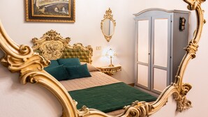Een slaapkamer met een grote, sierlijke spiegel, een groene spreidek en een nachtkastje met een lamp.