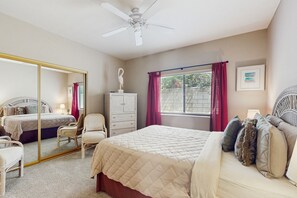 A bedroom with a bed, a chair, a wardrobe, a mirror, a window with curtains, and a ceiling fan. - Desert Bliss with Mountain Views & a Sparkling Private Pool. (Palm Desert)