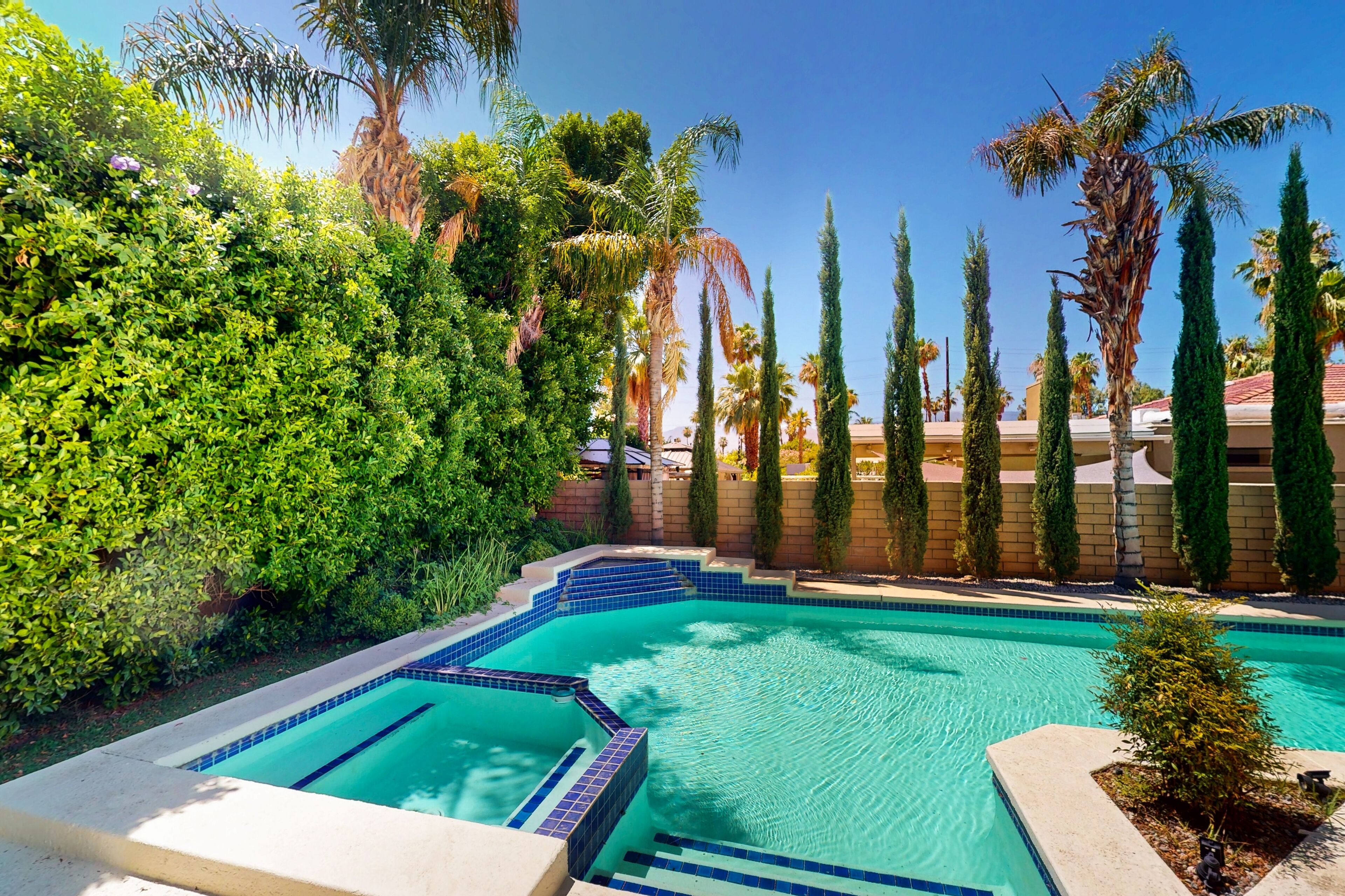 A swimming pool with a tiled edge, surrounded by lush greenery and tall cypress trees.