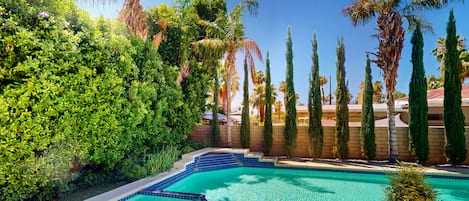 A swimming pool with a tiled edge, surrounded by lush greenery and tall cypress trees.