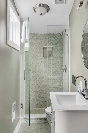 Un baño moderno con cabina de ducha de vidrio, un lavamanos blanco y un espejo grande.