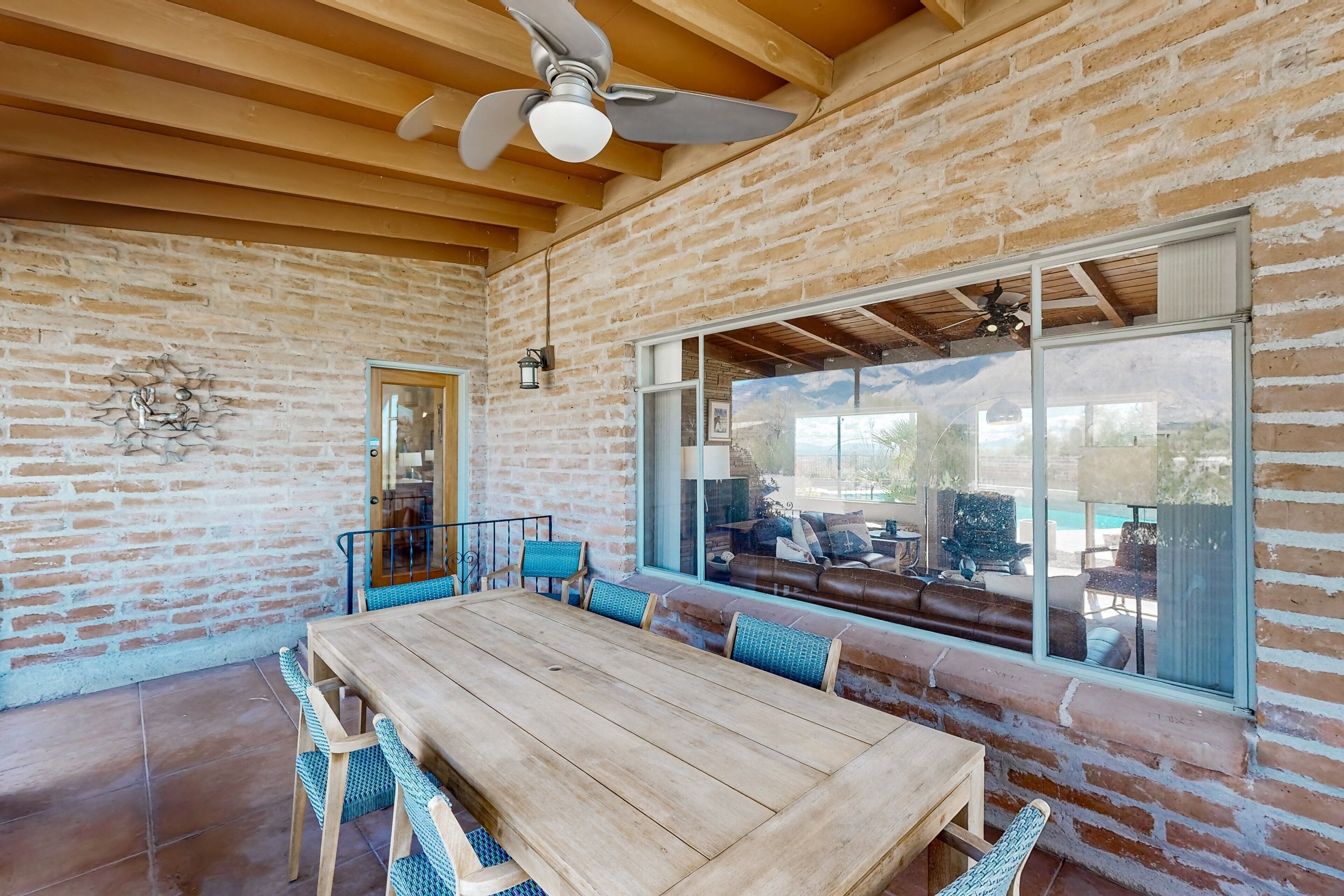 Une vaste terrasse dotée d’une table et de chaises en bois, d’un mur en briques et d’une grande fenêtre donnant sur une piscine.