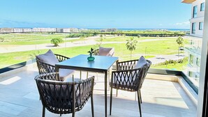 Balkon med bord og stole med udsigt over en golfbane og havet.