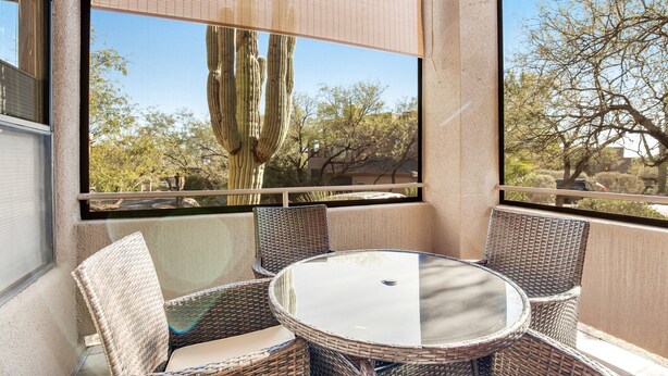 A balcony with wicker furniture and a glass table, overlooking a desert landscape with cacti and trees. - Radiant retreat with pool and hot tub access, sunroom, washer/dryer, gym, & AC (Tucson)