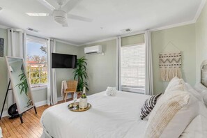 Quarto com cama, televisão, ventoinha no teto e janela com persianas.