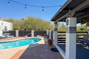 Un jardin avec une piscine, une pergola illuminée de guirlandes lumineuses, une table de patio et une vue sur les montagnes.