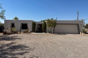 Une maison moderne de plain-pied, dotée d’un garage, d’une allée et d’un petit jardin planté d’espèces végétales typiques des régions désertiques.