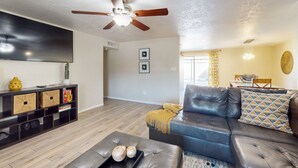 Ein modernes Wohnzimmer mit Ledersofa, Deckenventilator, Flachbildfernseher und Holzboden.
