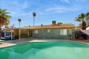 Ein Wohnhaus mit Swimmingpool, Sitzgelegenheiten im Freien und einer überdachten Terrasse.