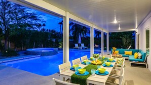 Un espace extérieur aménagé pour les repas, avec une piscine, des meubles blancs et une vue sur la piscine et les arbres.