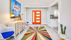 Un couloir moderne agrémenté d’un tapis coloré, d’une chaise blanche, d’un bureau avec une lampe et d’une porte d’un orange vif.