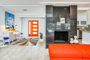 Ein modernes Wohnzimmer mit einem leuchtend orangefarbenen Sofa, einem farbenfrohen Teppich und einem minimalistischen Design.