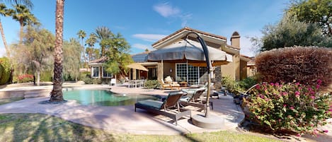 A pool area with lounge chairs, a covered patio, and a house with a tiled roof.
