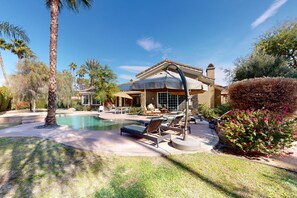 A pool area with lounge chairs, a covered patio, and a house with a tiled roof. - Luxurious, dog-friendly home w/ a home office, private pool, spa & gas grill (Rancho Mirage)