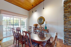 A dining area with a round glass table, wooden chairs, a decorative mirror, and a stone accent wall. - Luxurious, dog-friendly home w/ a home office, private pool, spa & gas grill (Rancho Mirage)