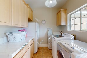 A compact kitchen with wooden cabinets, a refrigerator, a washing machine, and a dryer. - Luxurious, dog-friendly home w/ a home office, private pool, spa & gas grill (Rancho Mirage)