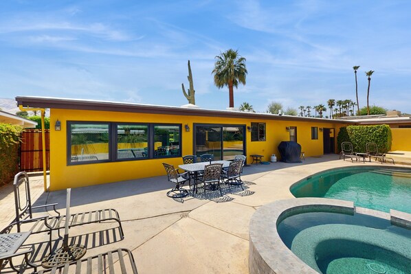 Un bâtiment jaune avec une piscine, des espaces de détente en plein air et des palmiers.