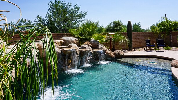 Una piscina con cascada, rodeada de rocas y plantas.