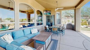 Un patio exterior con un sofá azul, mobiliario de mimbre, una mesa de madera y un televisor montado en la pared.