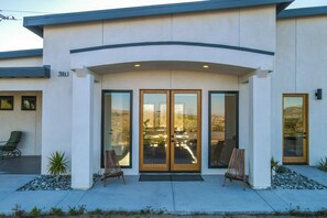 A modern building with a curved entrance, large glass doors, and a small outdoor seating area with two chairs and a bench.