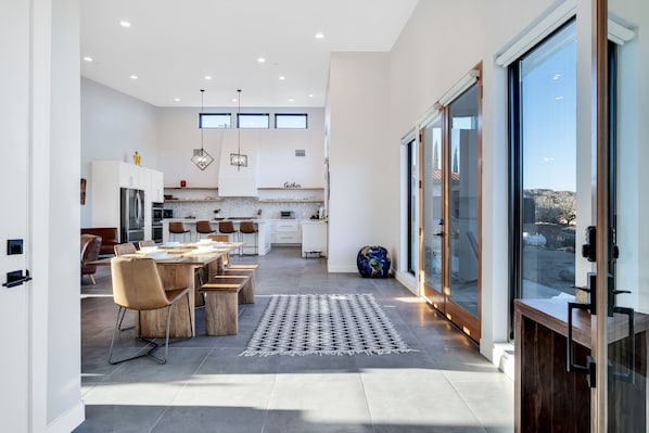 A modern kitchen with a dining area, large windows, and a view of the outdoors.