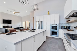 Una cocina moderna con armarios blancos, una isla grande, electrodomésticos de acero inoxidable y un ventilador de techo.