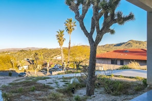 A residential area with a house featuring a red roof, palm trees, and a clear view of distant mountains.