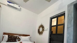 A bedroom with a wooden bed, white bedding, a ceiling fan, an air conditioning unit, a decorative mirror, and a black door with glass panels.