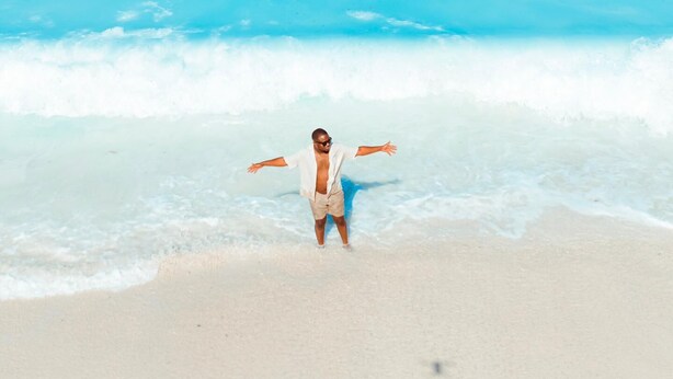 A beach with clear blue water and a person standing in the sand.