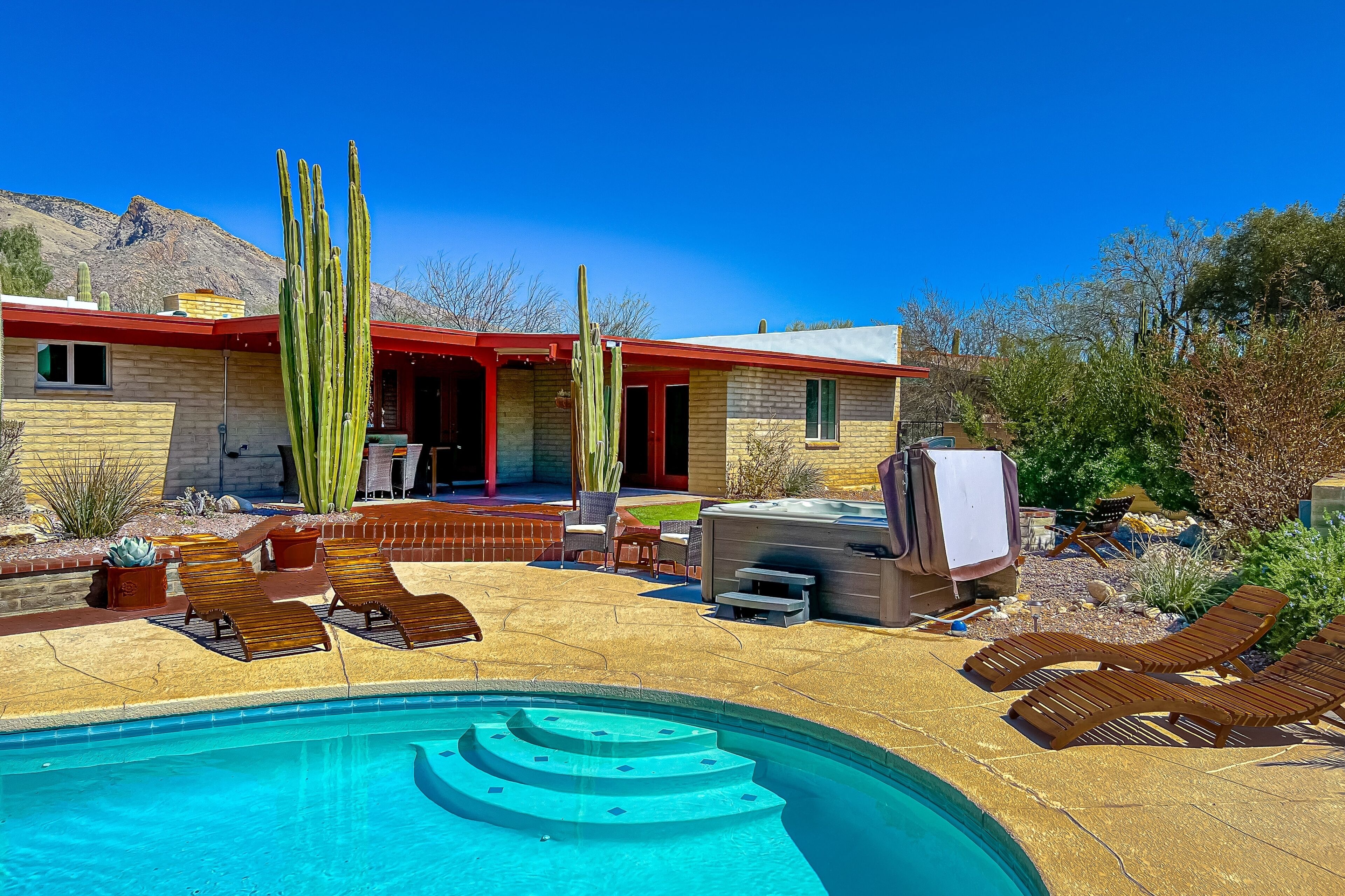 A pool area with lounge chairs, a hot tub, and cacti.