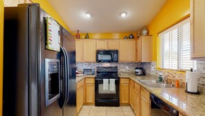 A kitchen with wooden cabinets, a black refrigerator, a microwave, an oven, a dishwasher, and a window with blinds. - Desert oasis with an enclosed yard, firepit, washer/dryer, and central AC (Gilbert)