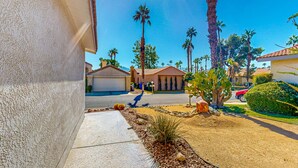 A residential street with houses, palm trees, and a clear sky. - Gated community home with 2 pools, hot tubs, private patio, AC, & W/D (Palm Desert)