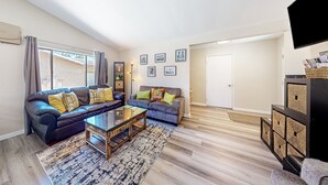 A living room with two sofas, a coffee table, and a TV stand. - Gated community home with 2 pools, hot tubs, private patio, AC, & W/D (Palm Desert)