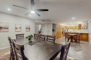 Ein Essbereich mit einem großen Holztisch und Stühlen, einem Deckenventilator und einer Küche im Hintergrund.
