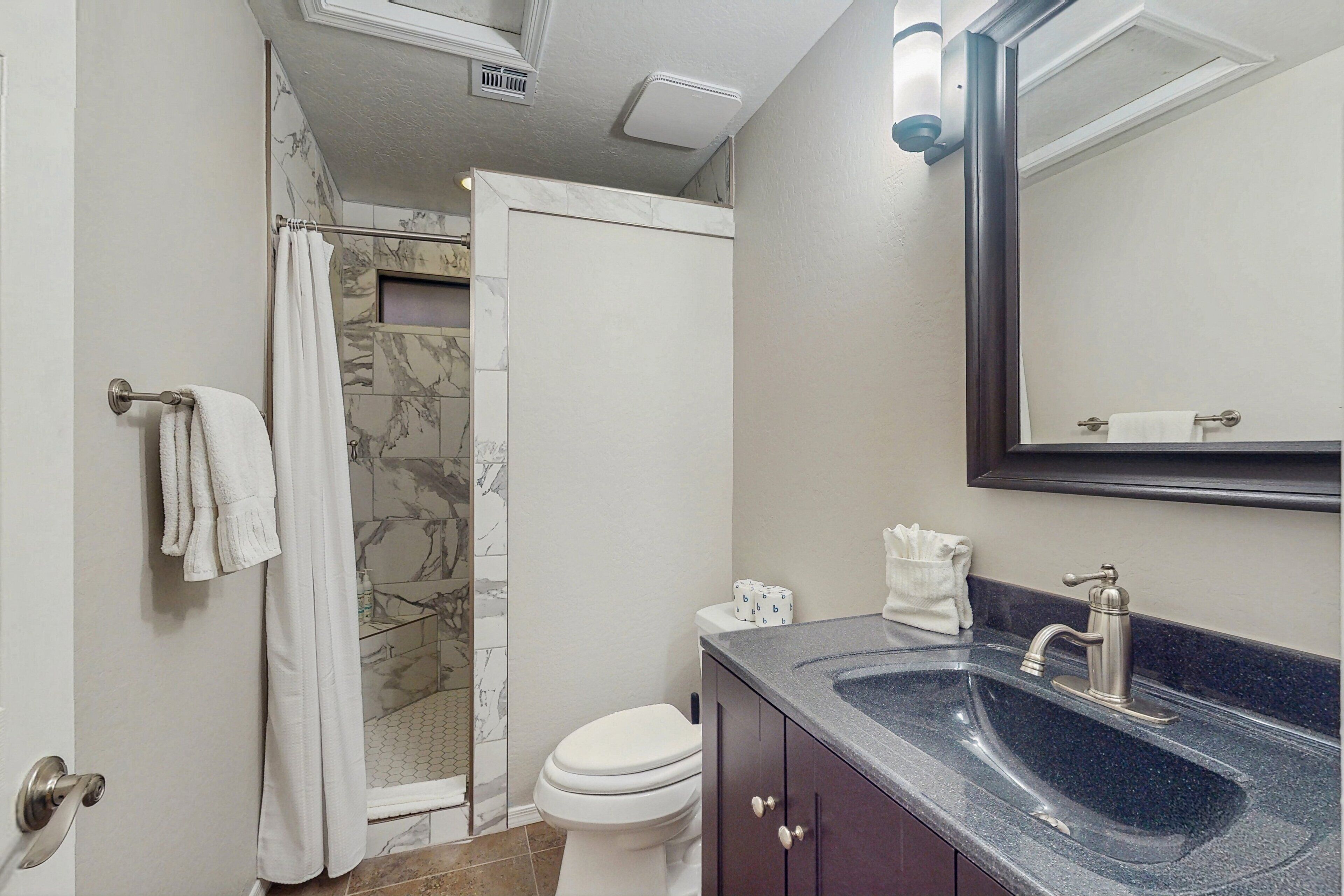 A bathroom with a shower, toilet, sink, and a mirror.