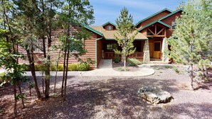 Un chalet doté d’une entrée en pierre, d’une façade en bois et d’une allée de gravier bordée d’arbres.