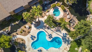 A large outdoor swimming pool with multiple sections and lounge chairs, surrounded by landscaped gardens and a small stream. - Serene Condo with pool, duck ponds and washer/dryer (Indio)
