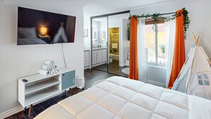A modern bedroom with a large bed, a TV, a white dresser, and a sliding door leading to a bathroom. - Serene Condo with pool, duck ponds and washer/dryer (Indio)