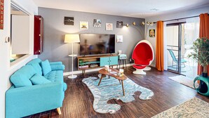 A modern living room with a blue sofa, a red chair, a flat-screen TV, and a wooden coffee table. - Serene Condo with pool, duck ponds and washer/dryer (Indio)