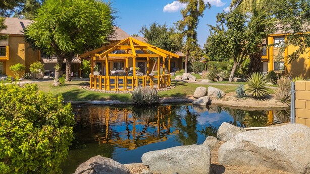 A yellow gazebo with a pond, surrounded by rocks and greenery. - Serene Condo with pool, duck ponds and washer/dryer (Indio)