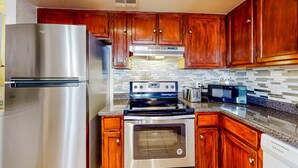 A kitchen with wooden cabinets, a stainless steel refrigerator, a stove, an oven, and a microwave. - Gated-entry condo with central location, central AC, & private W/D (Phoenix)