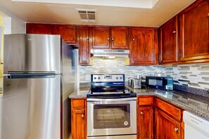 A kitchen with wooden cabinets, a stainless steel refrigerator, a stove, an oven, and a microwave. - Gated-entry condo with central location, central AC, & private W/D (Phoenix)