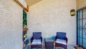 A balcony with two wicker chairs and a small table, a textured wall, a lantern, and a glass door. - Gated-entry condo with central location, central AC, & private W/D (Phoenix)