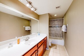 A bathroom with a white sink, wooden cabinets, a large mirror, a shower with a marble wall, and a toilet. - Gated-entry condo with central location, central AC, & private W/D (Phoenix)