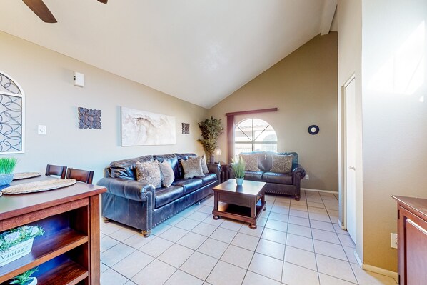 A spacious living room with a dark leather sofa, a wooden coffee table, and a dining area with a wooden table and chairs. - Gated-entry condo with central location, central AC, & private W/D (Phoenix)