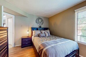 A bedroom with a bed, a nightstand, a dresser, a wall art piece, and a window with blinds. - Gated-entry condo with central location, central AC, & private W/D (Phoenix)